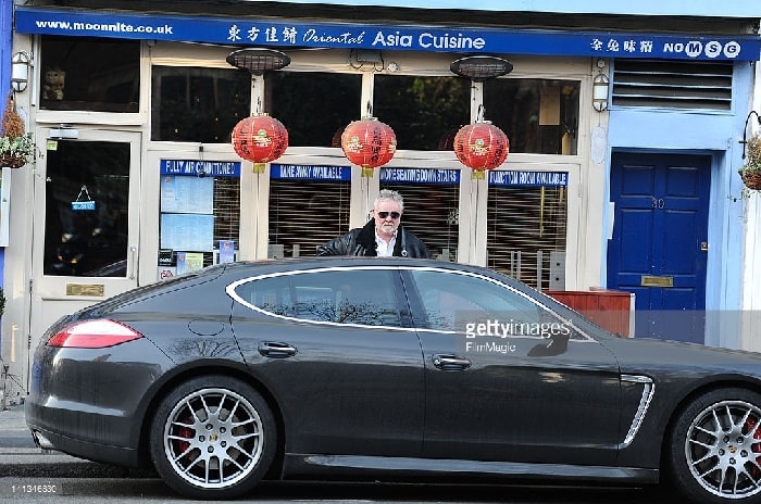 Roger Taylor in front of a Asia Cuisine restaurant with his black Porsche Panamera